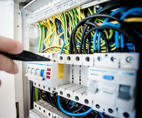 Hand of electrician working on a circuit breaker panel with colorful wires, ensuring safe electrical connections.